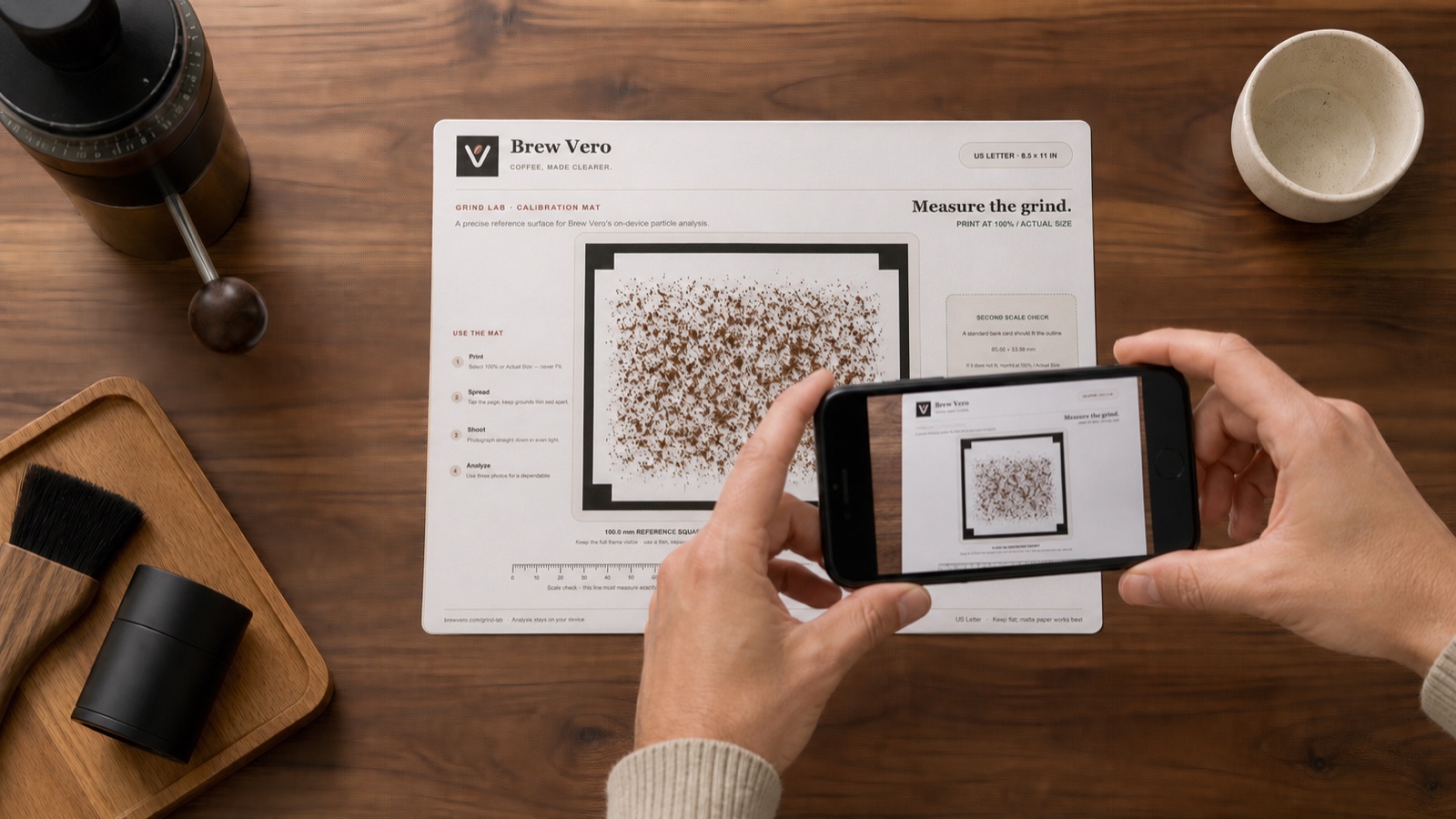 A phone camera framing coffee grounds inside the Baristuno mat’s continuous 100 mm reference square before analysis.