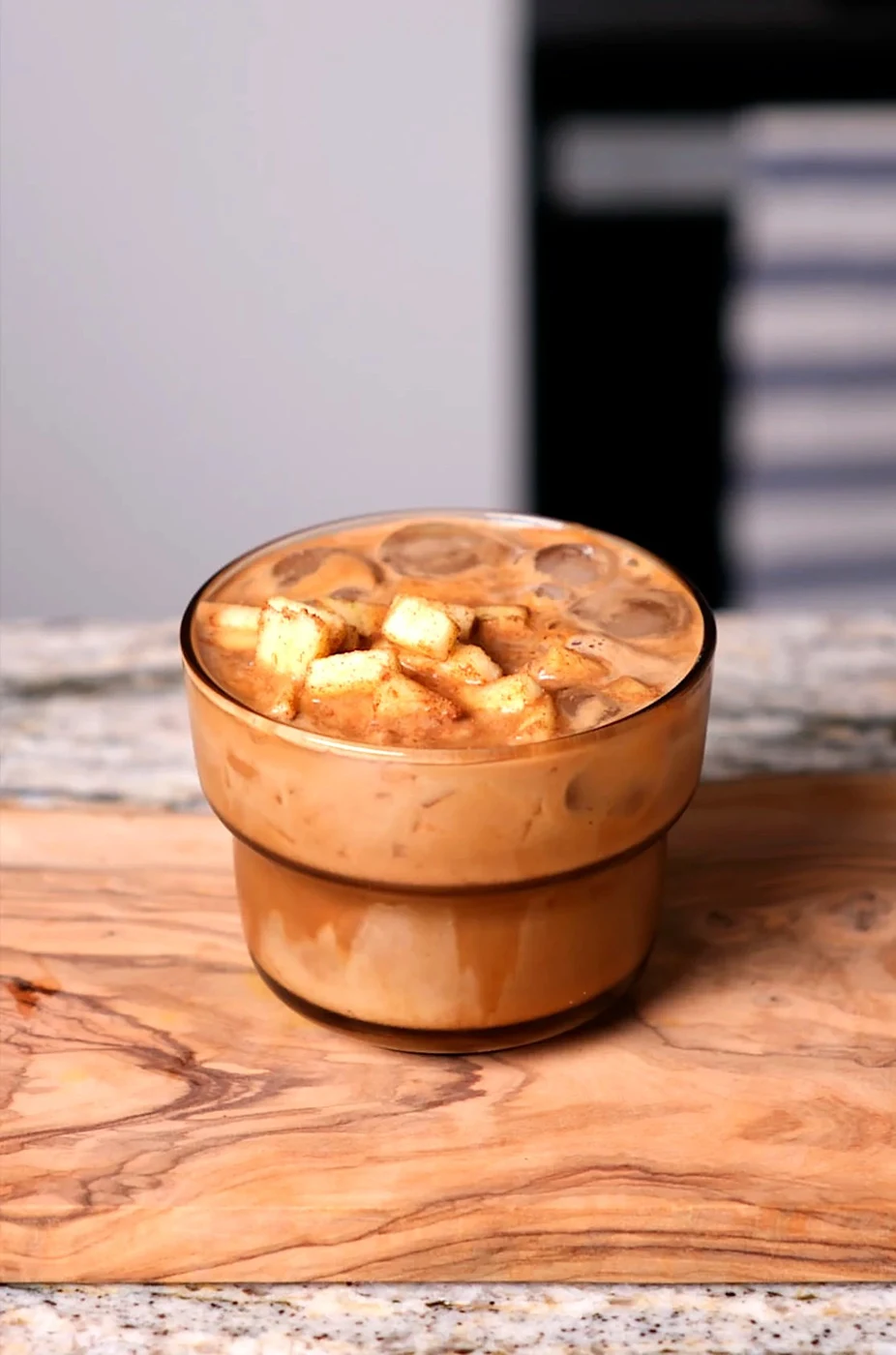 Iced Apple Cinnamon Latte in a glass, topped with cinnamon-coated diced apple
