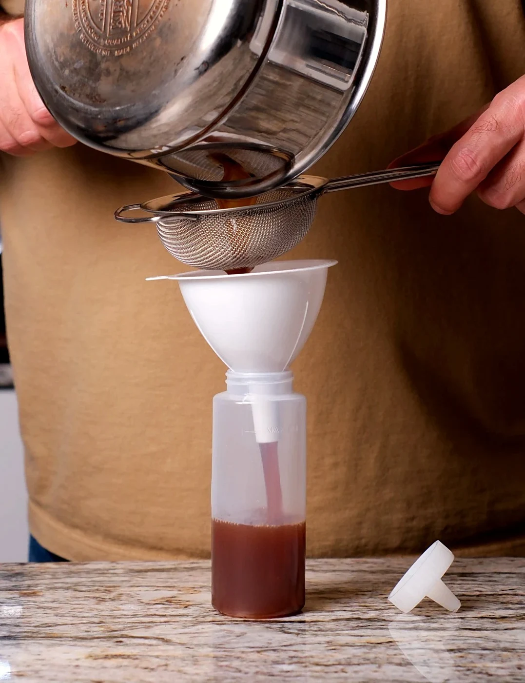 Apple cinnamon syrup being filtered through a sieve and funnel into a bottle