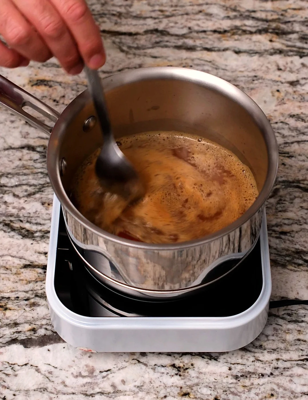 Spiced apple syrup being stirred in a small saucepan