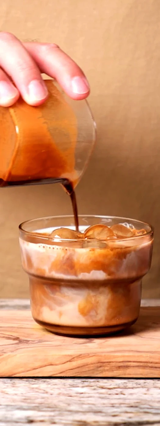 Sweetened espresso being poured over cold milk and ice