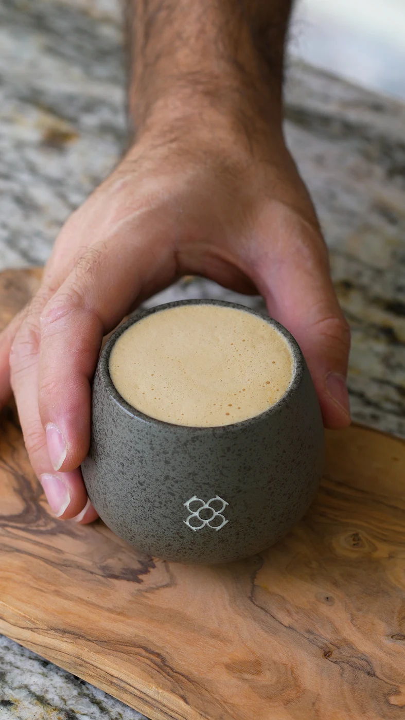 A creamy coffee held in a grey ceramic cup
